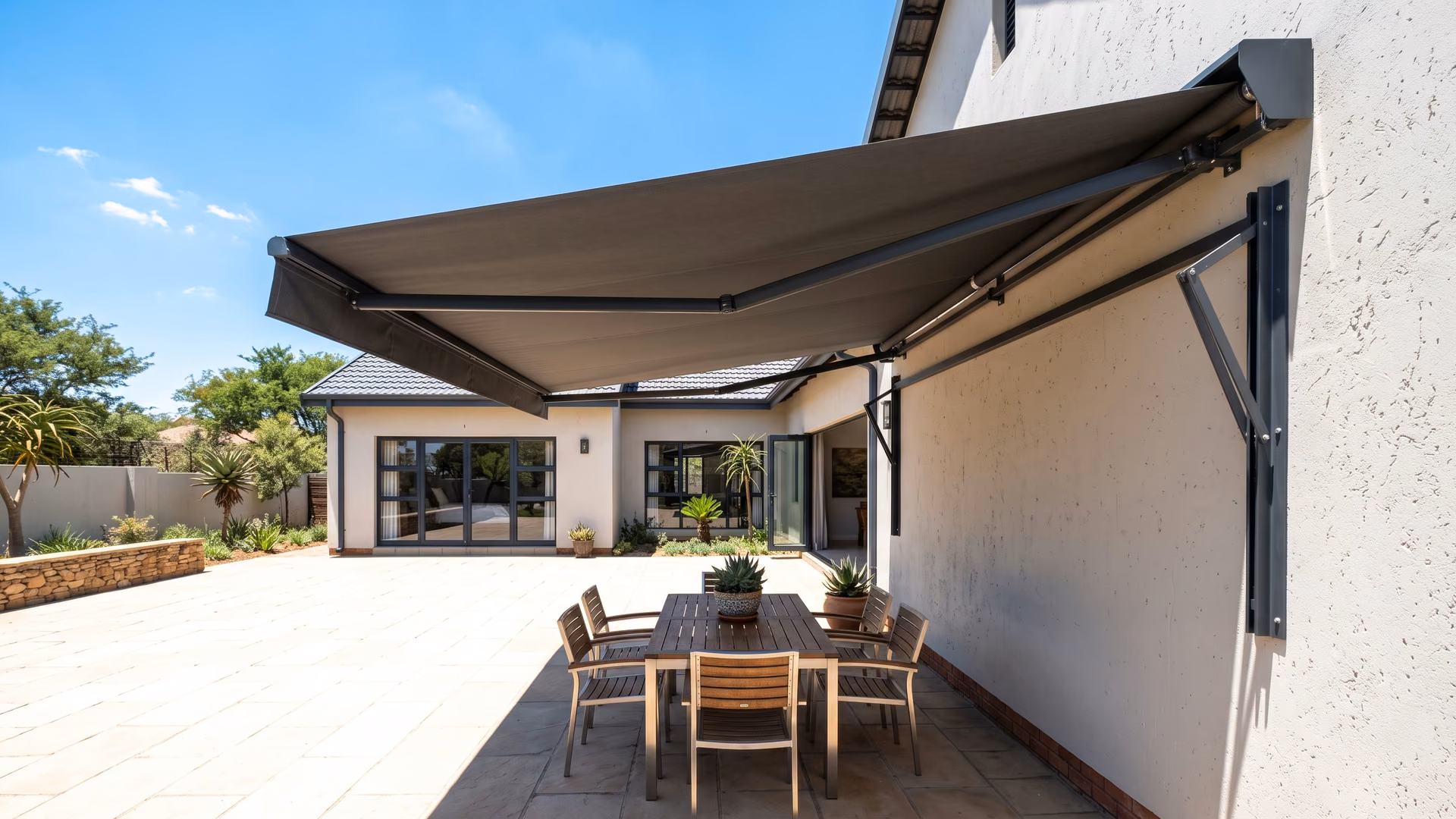 Folding-arm retractable awning extended over a paved patio at a Pretoria home in hard afternoon sun